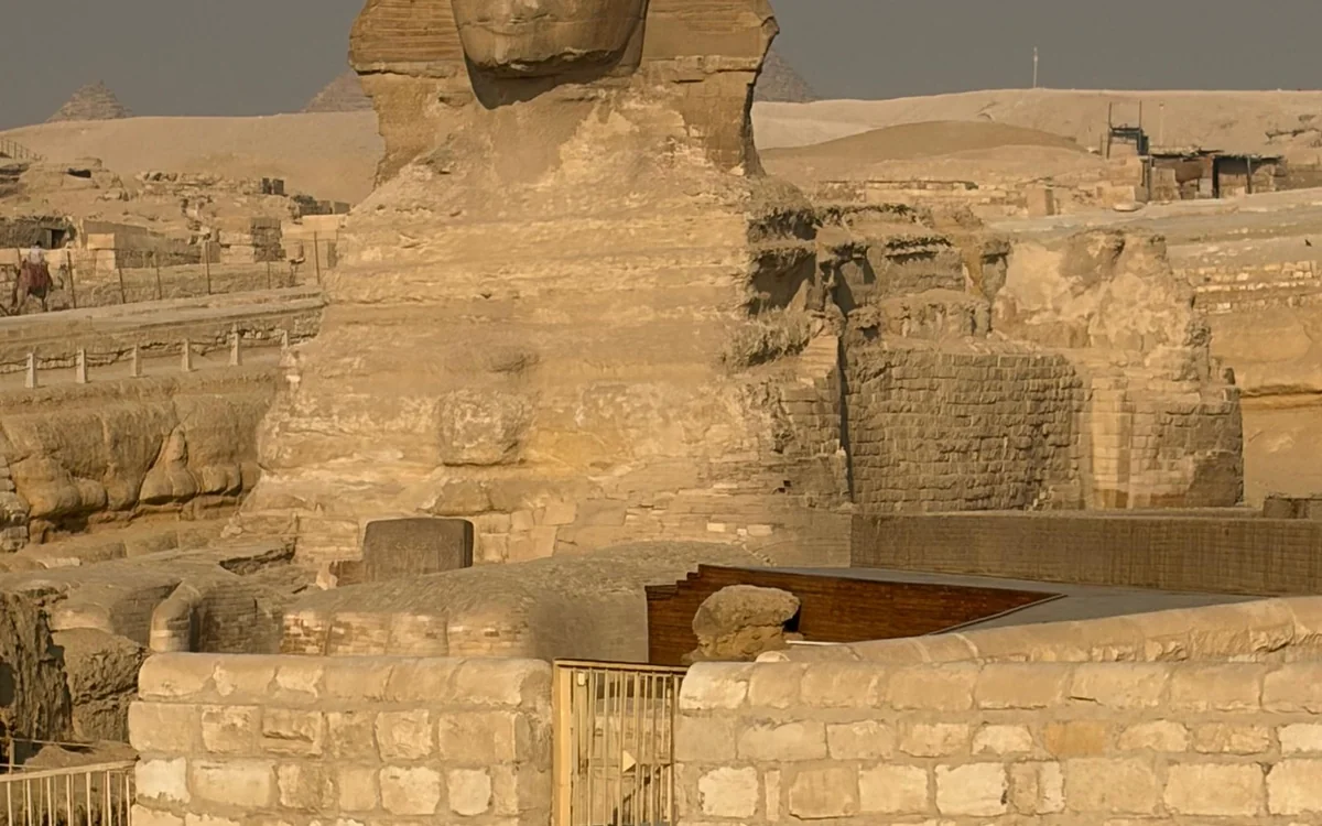 A camel and its handler on the sand in front of the Giza pyramids