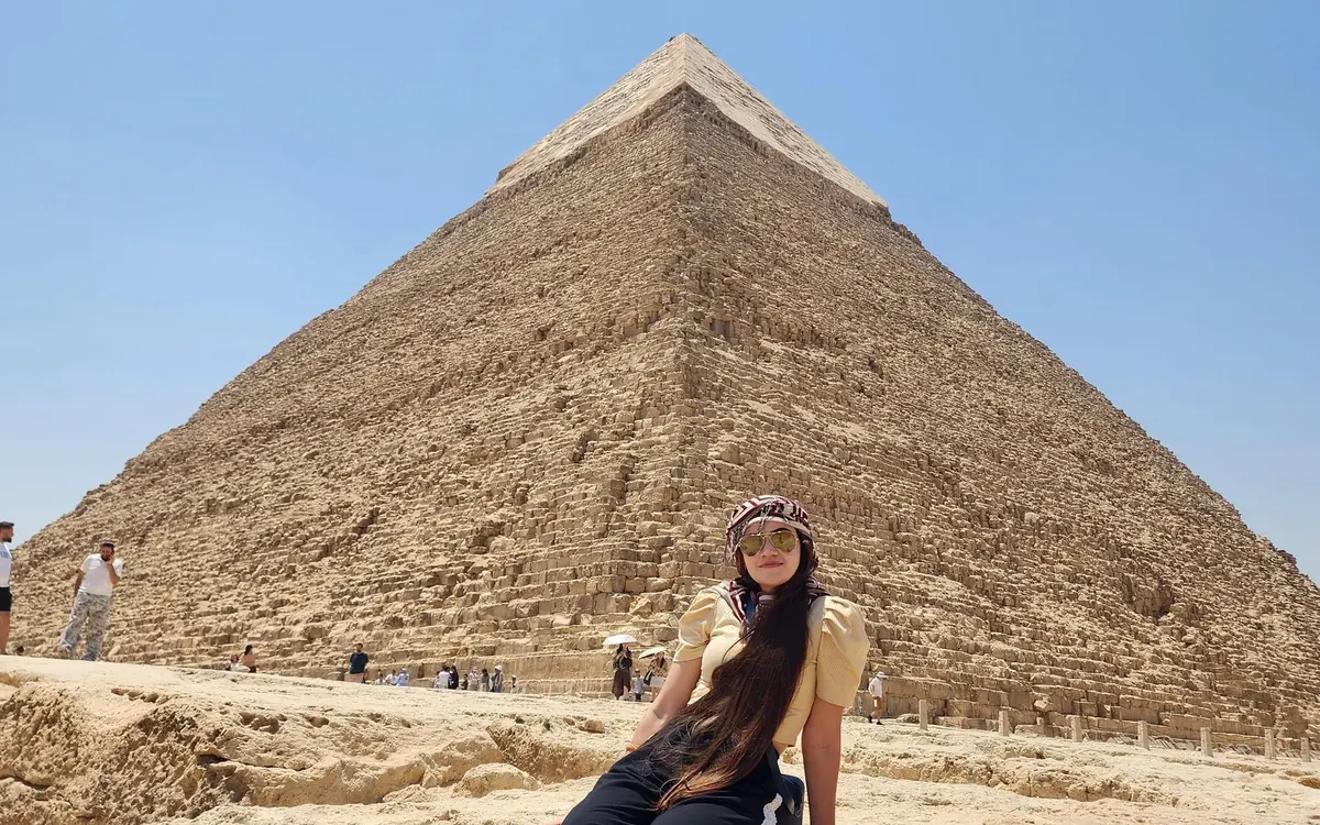 A camel and rider on the sand in front of the Pyramids of Giza, Egypt